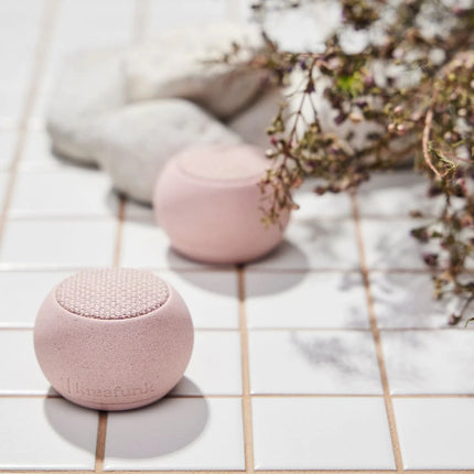 Draagbare Bluetooth speaker Ago Stone van Kreafunk rose buiten naast witte stenen