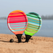 Beach tennisset veelkleurig in 2 racketten en 2 zwarte balletjes in het strandzand gestoken