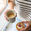 Bio servies Connect van Koziol  beker beige gevuld met koffie naast een taartje