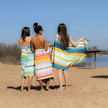 Hamamdoeken van Remember gewikkeld rond drie dames op het strand