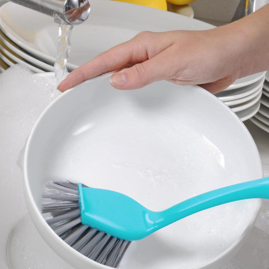 een blauwe afwasborstel waarmee er een wit bord word afgewassen 