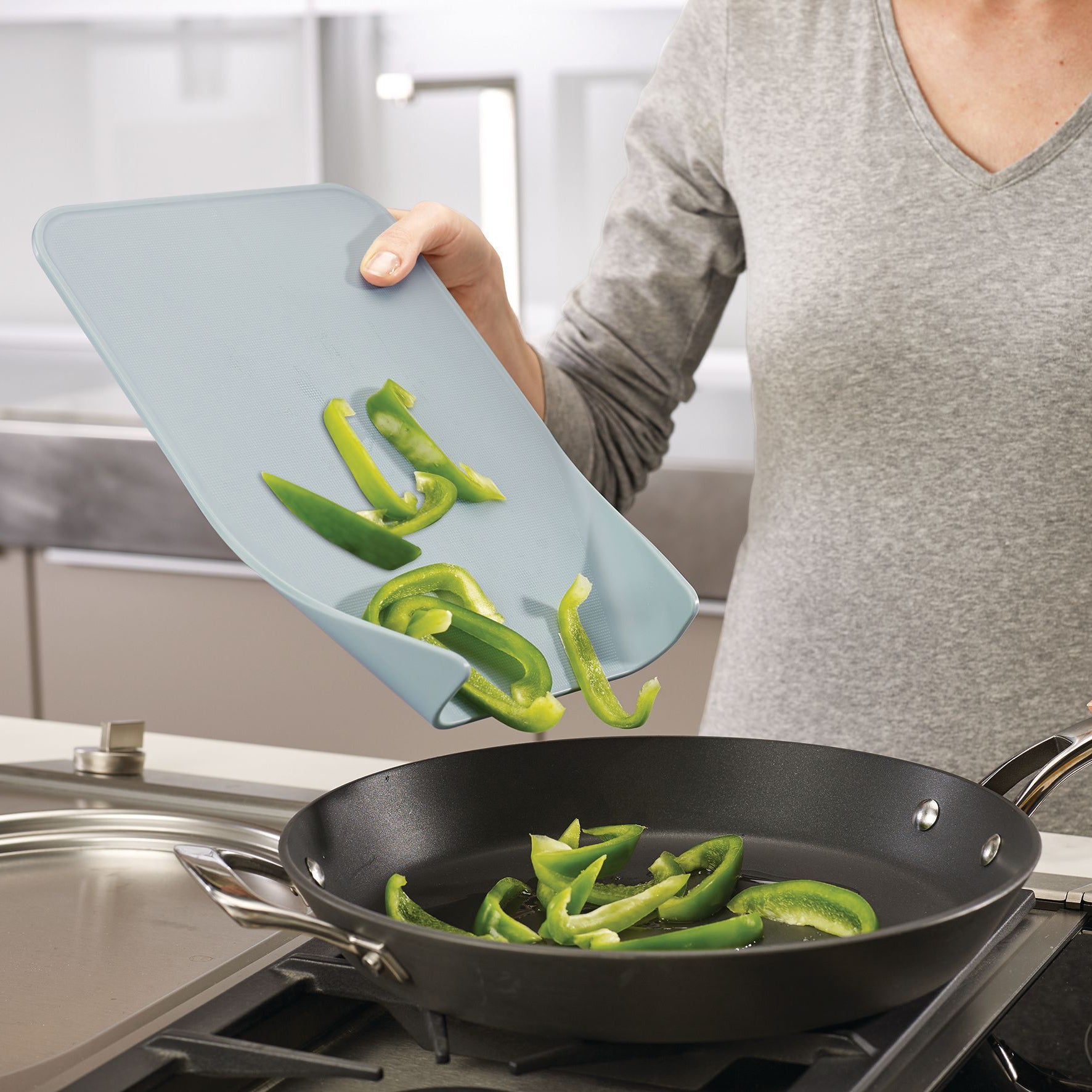 Snijplank Nest van Joseph Joseph waarmee groene paprika in een pan geschoven wordt door de versmalling op de plank