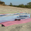 Strandlaken XXL Portoverde met vulbare zandzakjes van Remember op het strand met zonnebril en tijdschrift