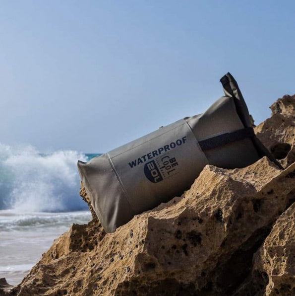 Grijze waterproof rugzak van 20 liter van BE Cool op de rotsen aan het strand